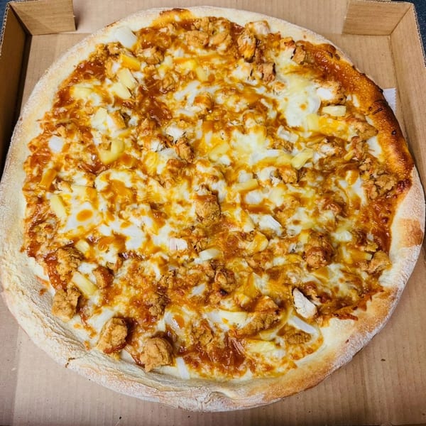 A whole BBQ chicken pizza with pineapple and onions in a cardboard box.