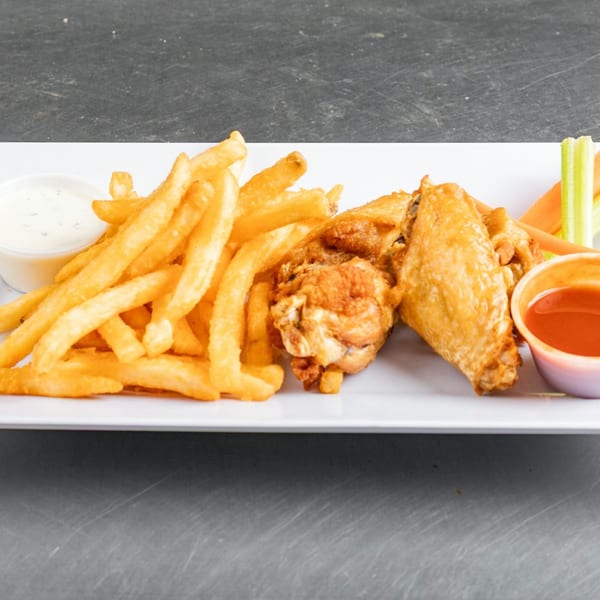 Crispy fried chicken wings, golden french fries, ranch, hot sauce, carrots, and celery on a white plate.