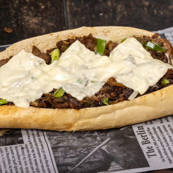 A close-up of a cheesesteak sandwich with melted white cheese, meat, and green peppers.